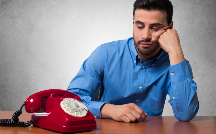 A man looks frustrated sitting next to an unused red rotary phone, symbolizing a no call, no show situation.